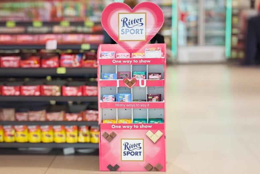 Pink Ritter Sport chocolate display in a store, heart-shaped top, shelves filled with colorful bars