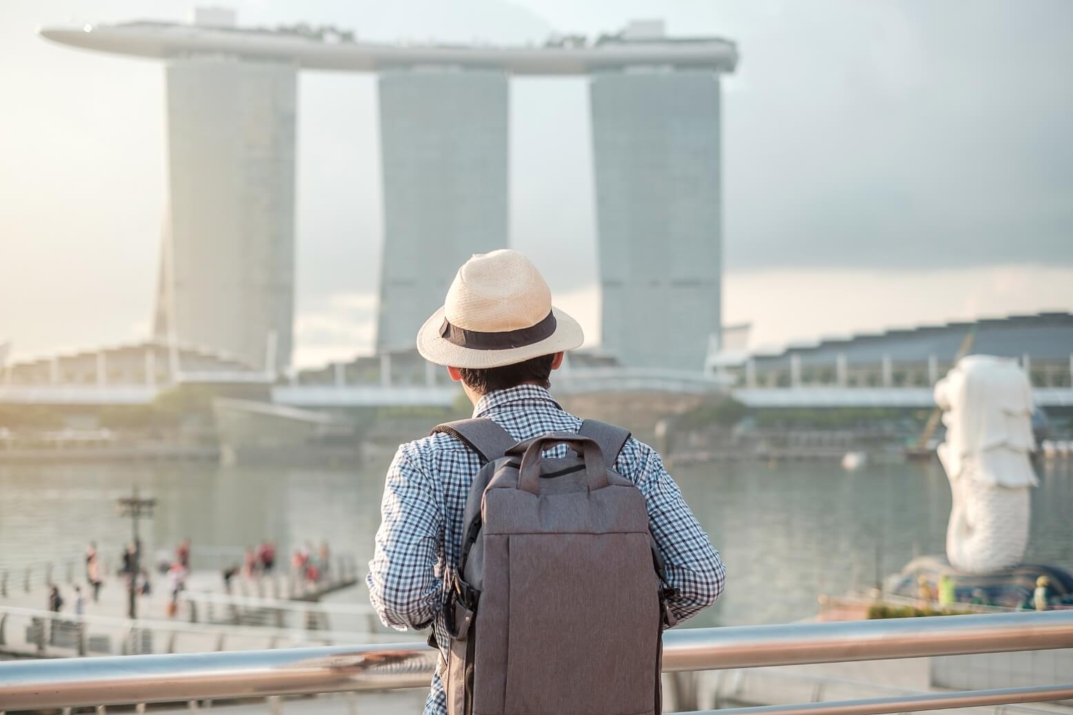 Back view of a traveler with a gray backpack and white hat looking toward Marina Bay Sands in Singapore.