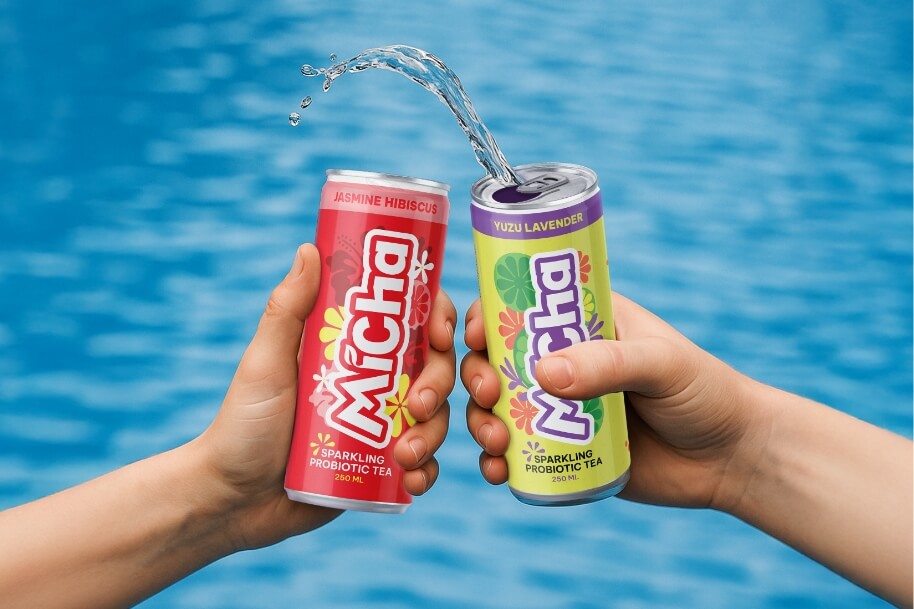 Two hands hold two colorful cans of probiotic sparkling tea as water arcs between them, against a blue background (jasmine hibiscus flavor on red can, yuzu lavender on green-purple can).