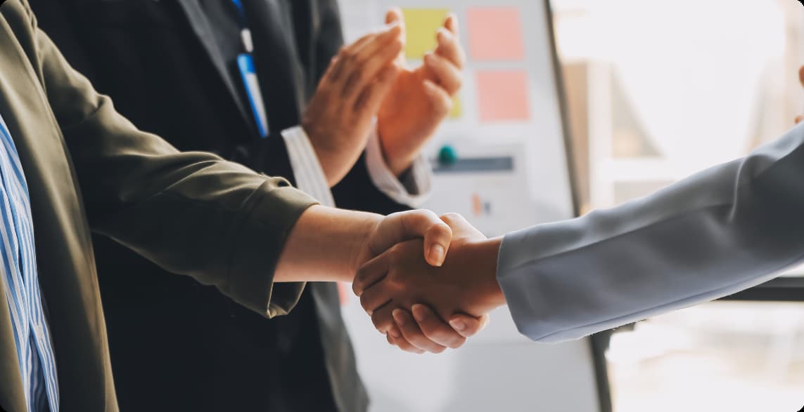 Two businesspeople shake hands in a meeting, signaling an agreement or partnership.