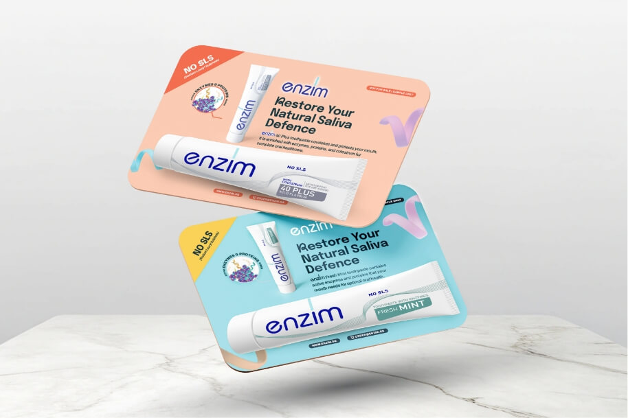 Two Enzim toothpaste sachets on pastel angled cards (peach and blue) promoting 'Restore Your Natural Saliva Defence' and 'Fresh Mint' flavors.