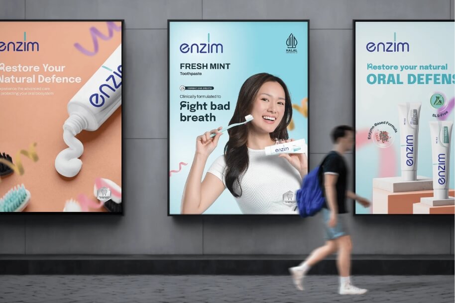 Advertising posters for Enzim toothpaste on a wall; center poster shows a smiling woman with a toothbrush promoting Fresh Mint toothpaste (toothpaste brand Enzim).