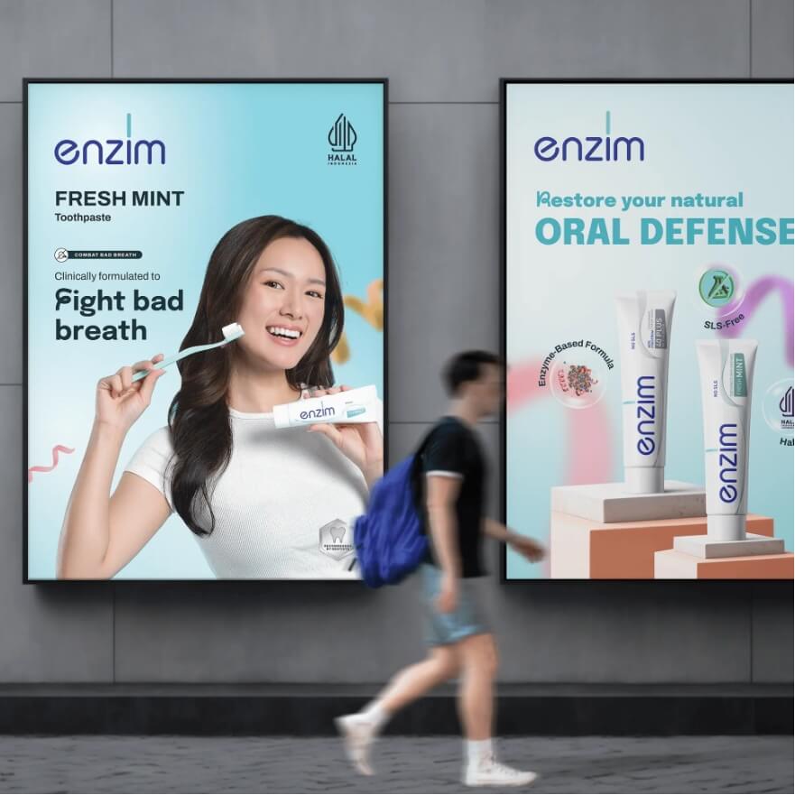 Two Enzim toothpaste posters on a gray wall; a smiling woman holds a Fresh Mint tube and toothbrush beside the ad text.