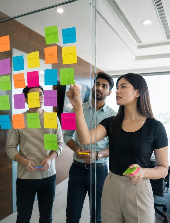 Team members place colorful sticky notes on a glass wall during a brainstorming session.